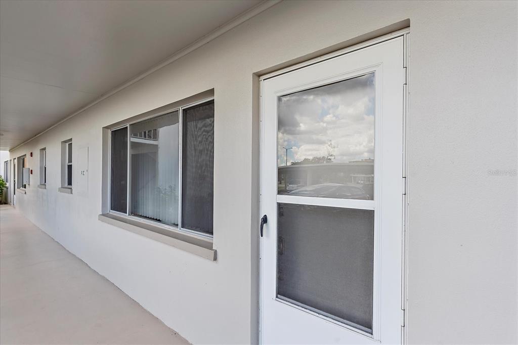 A white exterior wall features a storm door and a window along a covered walkway — 4210 IRONWOOD CIRCLE UNIT 103J, BRADENTON, FL