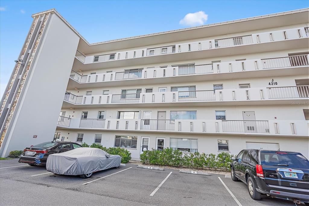 A multi-story apartment building exterior features white balconies and a parking lot in front — 4210 IRONWOOD CIRCLE UNIT 103J, BRADENTON, FL