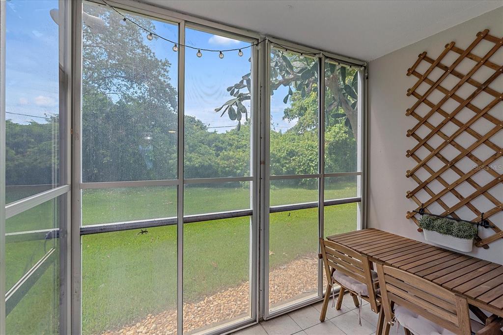 A screened-in porch features a wooden table, a wall-mounted trellis, and views of a yard — 4210 IRONWOOD CIRCLE UNIT 103J, BRADENTON, FL