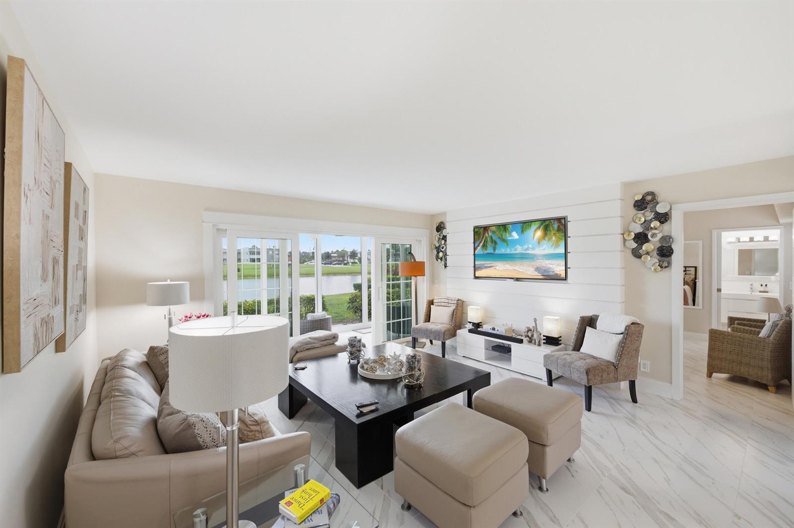 A living room features a white shiplap wall, a dark coffee table, and sliding glass doors — 53 Piedmont B, Delray Beach FL 33484, DELRAY BEACH, FL