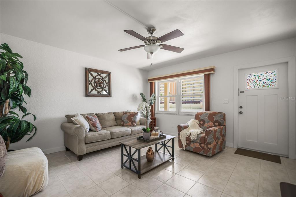 A living room features a beige sofa, patterned armchair, coffee table, and tile flooring — 4565 DUHME ROAD UNIT 102, ST PETERSBURG, FL