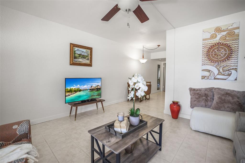 A living room features tile flooring, a ceiling fan, a television, and a coffee table — 4565 DUHME ROAD UNIT 102, ST PETERSBURG, FL