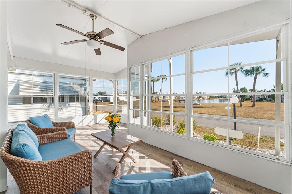 A sunroom features wicker furniture, wood-look flooring, a ceiling fan, and views of a pond — 107 TORTOLA WAY, NORTH PORT, FL