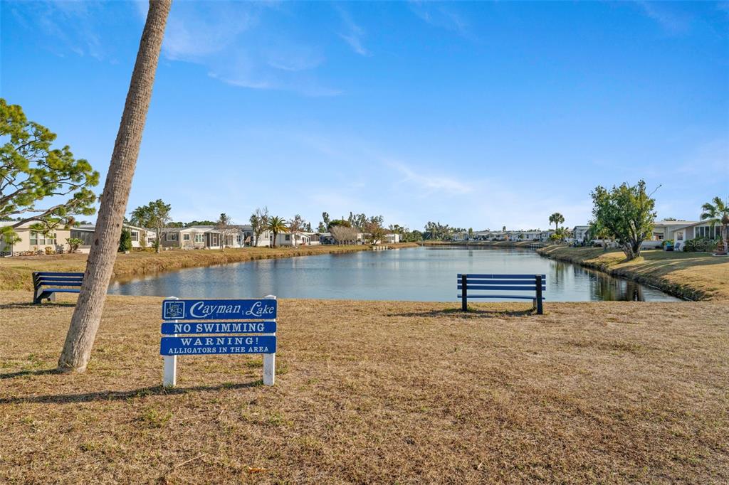 A lakefront view features a warning sign about alligators and two benches on grass — 107 TORTOLA WAY, NORTH PORT, FL