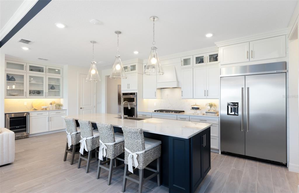 A modern kitchen features a dark blue island, white cabinetry, stainless steel appliances, and pendant lighting — 289 CRYSTAL WOOD DRIVE, WINTER GARDEN, FL