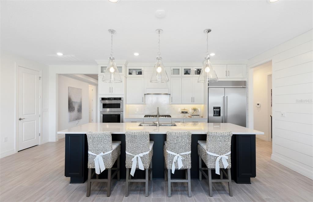 A modern kitchen features a large dark island with four woven chairs and white cabinetry — 289 CRYSTAL WOOD DRIVE, WINTER GARDEN, FL