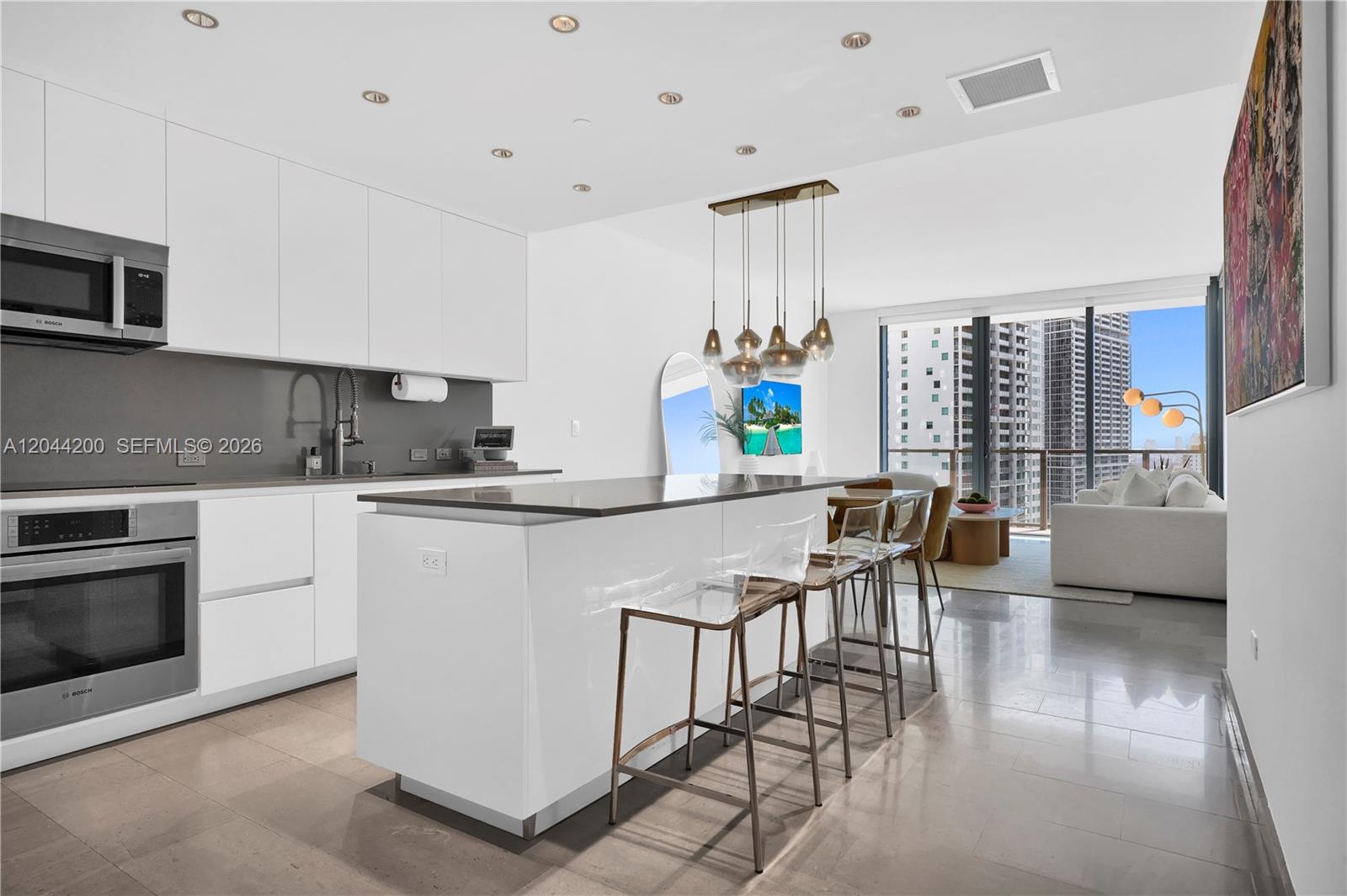 A modern kitchen features white cabinetry, a central island with bar stools, and floor-to-ceiling windows — 68 SE 6th St # 2005, Miami FL 33131, MIAMI, FL