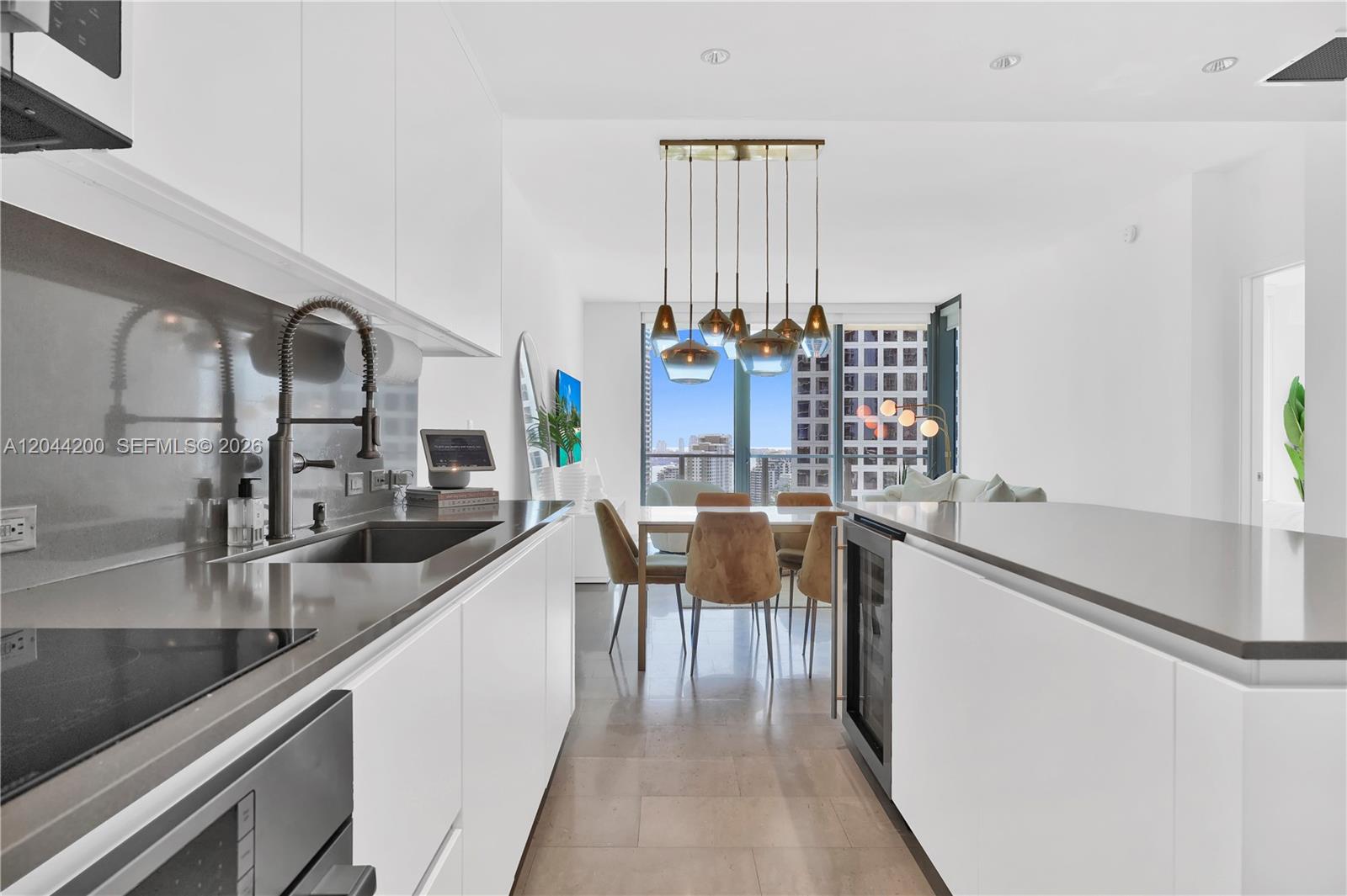 A modern kitchen with white cabinetry and gray countertops opens to a dining area — 68 SE 6th St # 2005, Miami FL 33131, MIAMI, FL