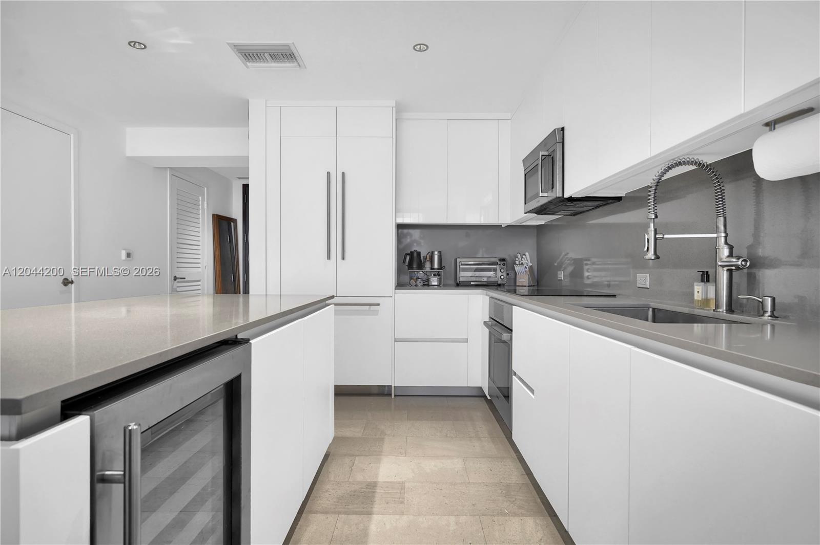 A modern white kitchen features a central island, stainless steel appliances, and gray countertops — 68 SE 6th St # 2005, Miami FL 33131, MIAMI, FL