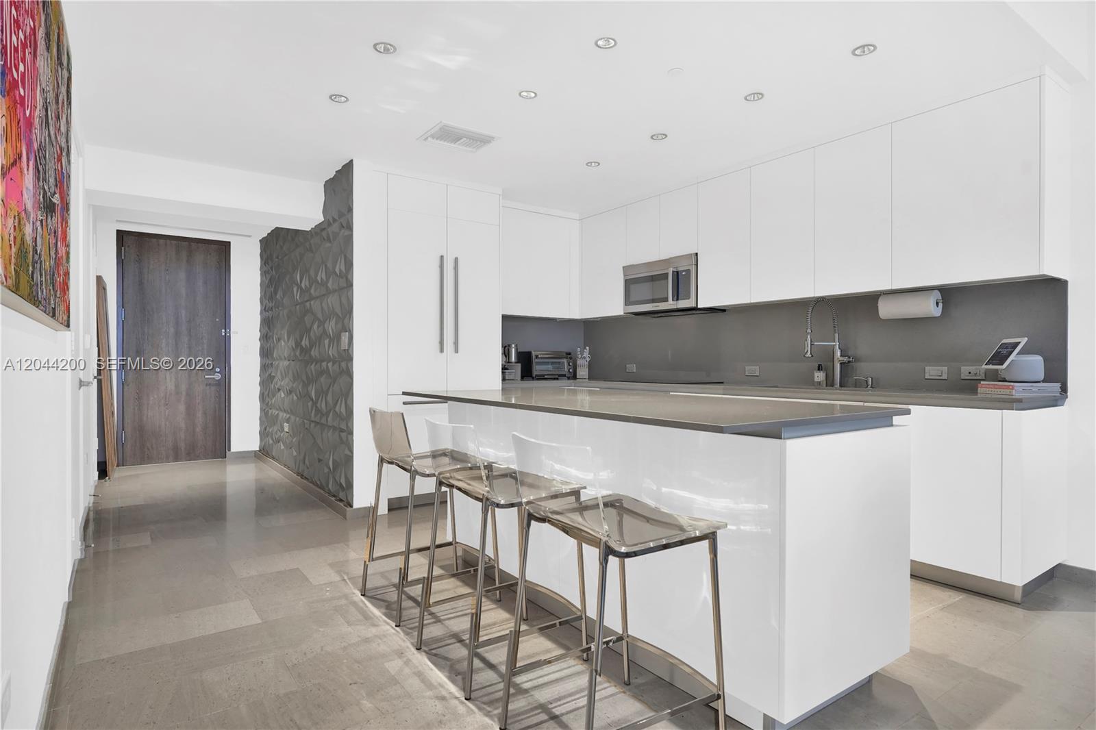 A modern kitchen features white cabinetry, a gray island with bar stools, and a textured wall — 68 SE 6th St # 2005, Miami FL 33131, MIAMI, FL