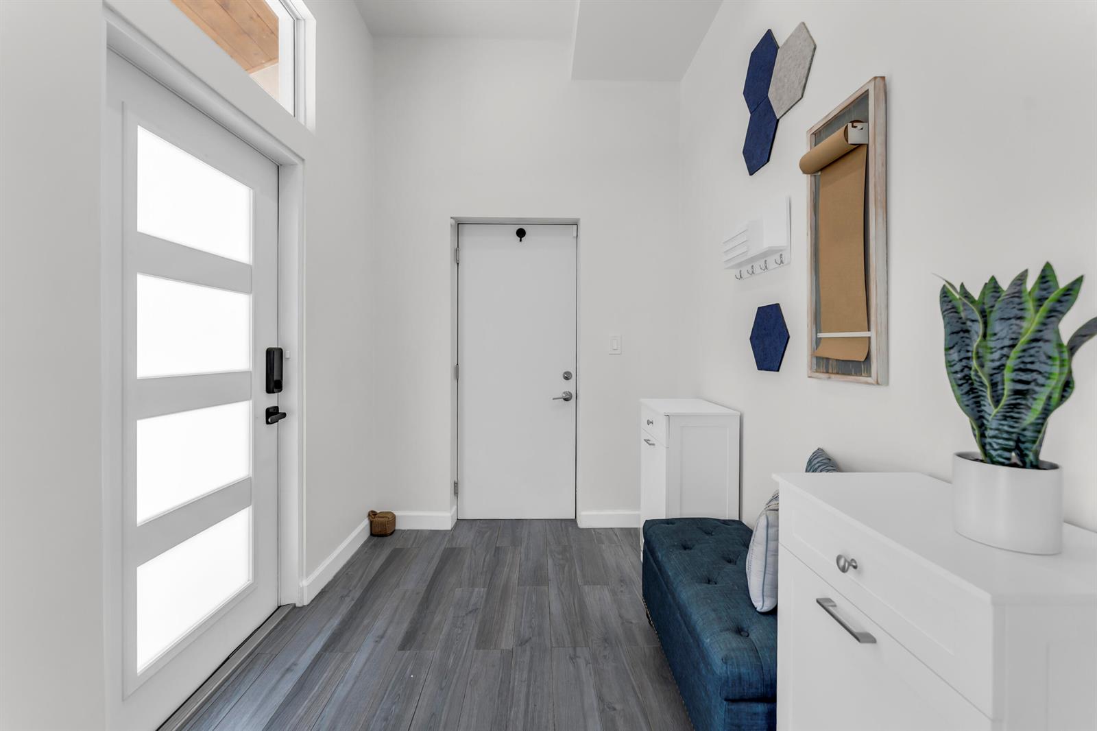 A modern entryway features white walls, dark wood-look flooring, a blue bench, and a door — 1472 SW 13th Street, Boca Raton FL 33486, BOCA RATON, FL