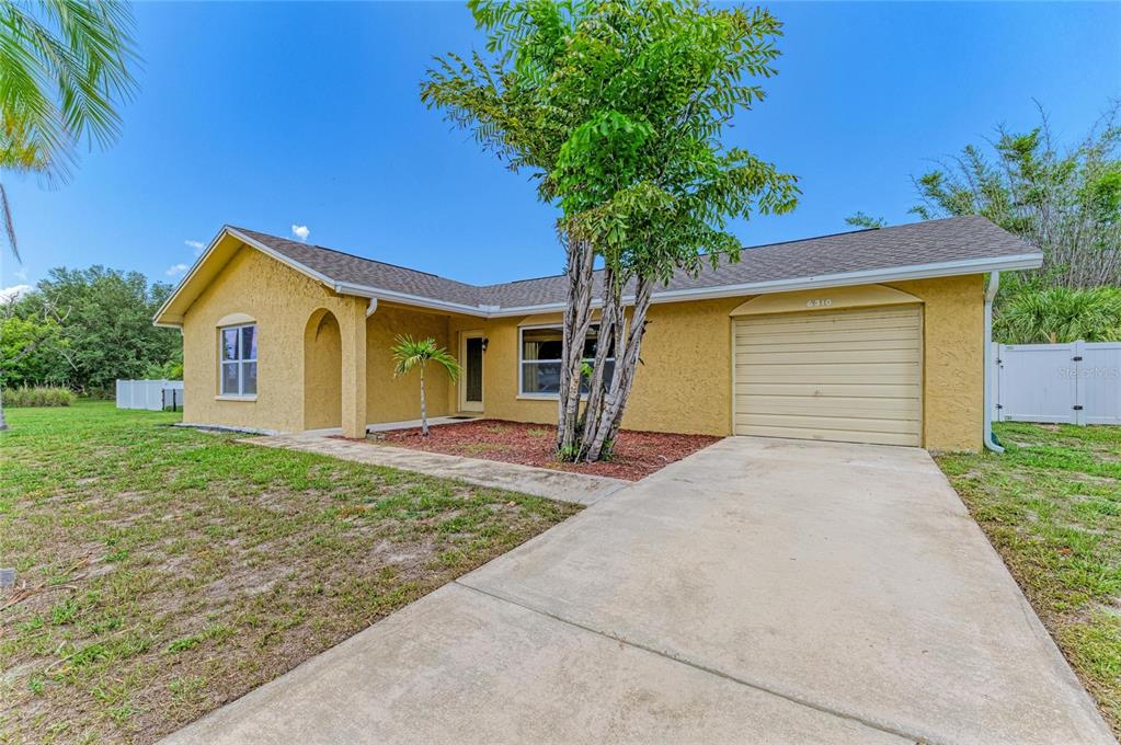 A single-story yellow stucco house with a concrete driveway and a front-facing garage — 6310 CUTLER TERRACE, PORT CHARLOTTE, FL