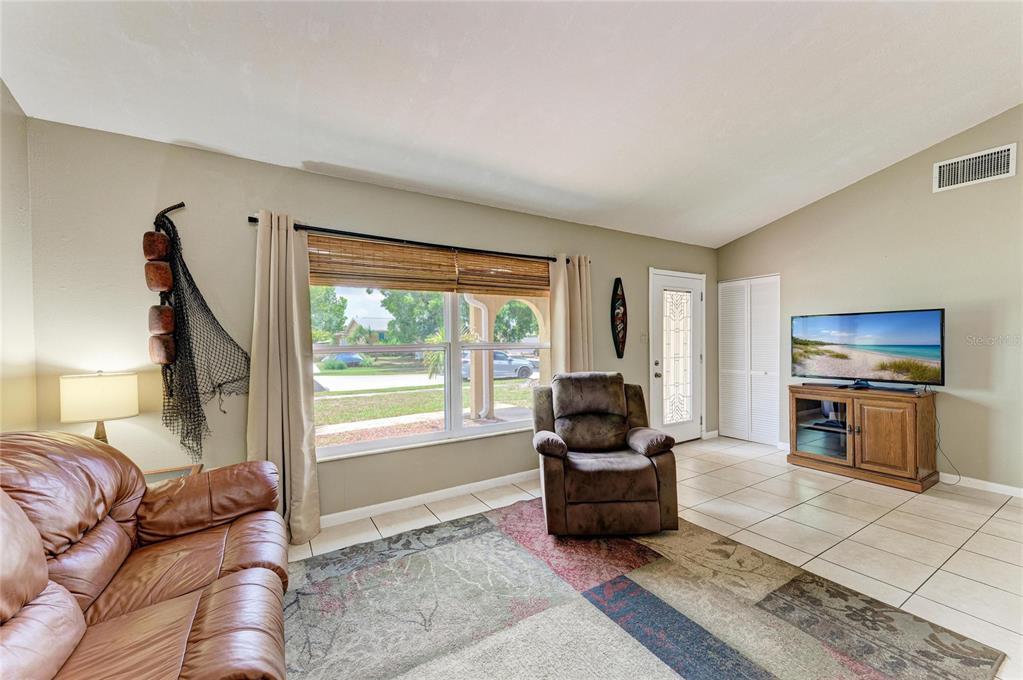 A living room features tile flooring, a brown leather sofa, a recliner, and a television — 6310 CUTLER TERRACE, PORT CHARLOTTE, FL