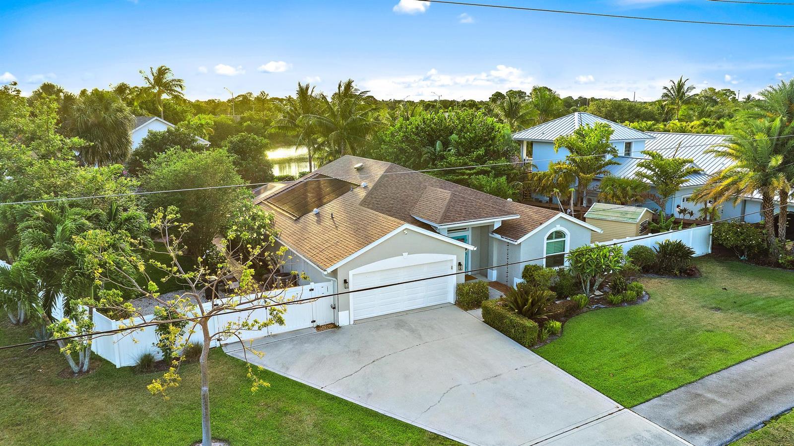 An aerial view of a single-story house with a garage, solar panels, and fenced yard — 15129 Harriet Avenue, Jupiter FL 33458, JUPITER, FL