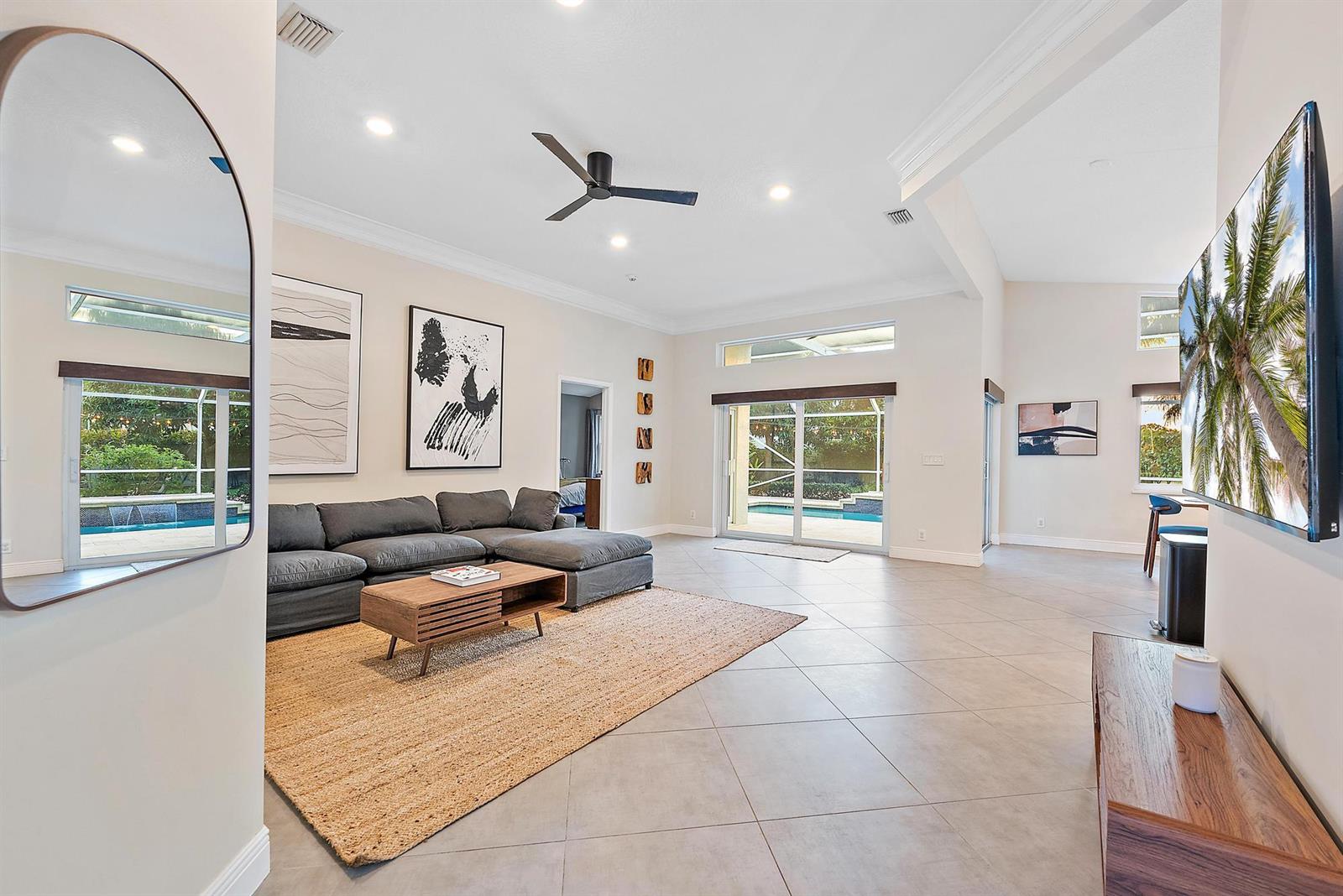 A spacious living room features a grey sectional sofa, a jute rug, and sliding glass doors — 15129 Harriet Avenue, Jupiter FL 33458, JUPITER, FL
