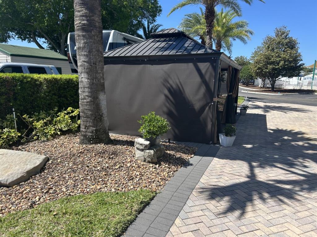 A dark metal gazebo with privacy curtains sits on a paved patio near a palm tree — 2505 PINE STREET, CLERMONT, FL