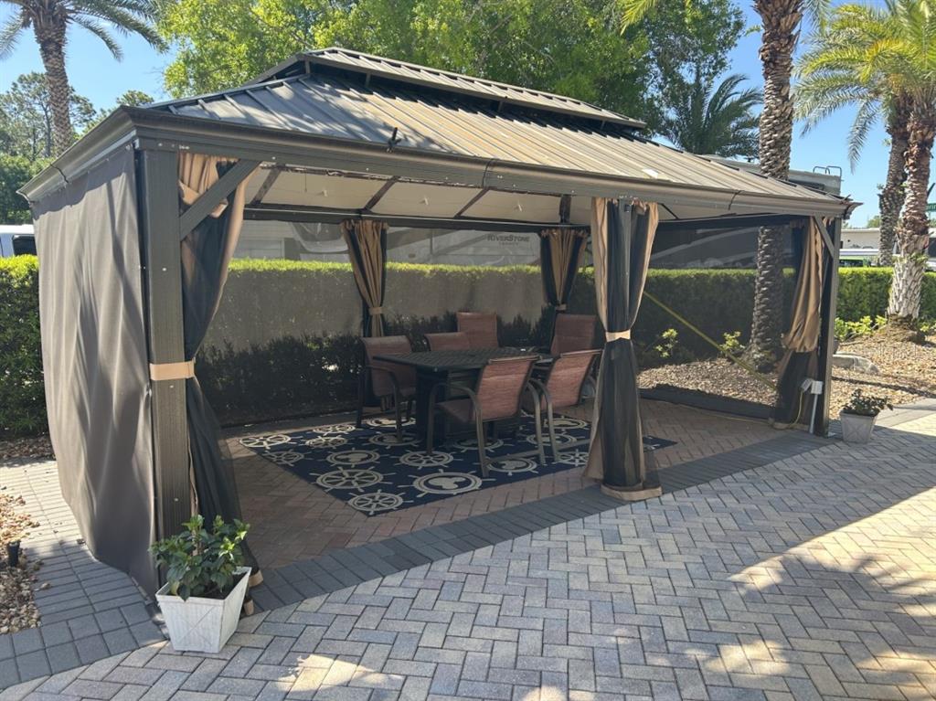 A metal-roofed gazebo with curtains and a dining set sits on a paved patio — 2505 PINE STREET, CLERMONT, FL