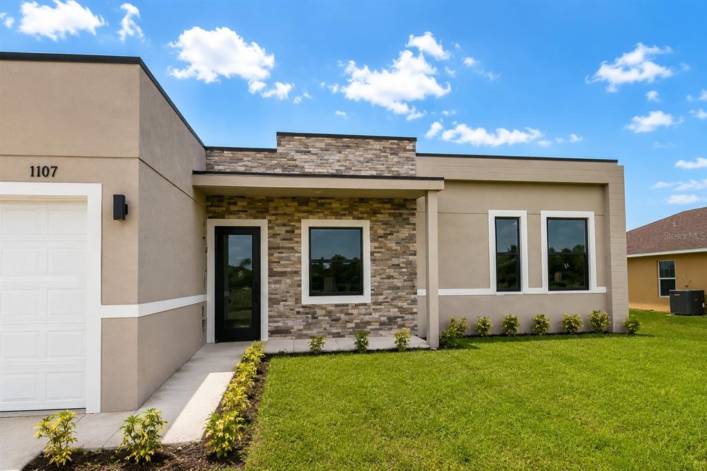 A modern single-story house exterior features tan stucco walls, stone veneer accents, and a garage — 1107 NW 9TH AVENUE, CAPE CORAL, FL