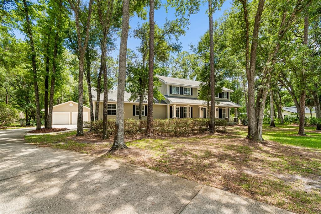 A two-story house with tan siding and a detached garage sits among many tall trees — 27708 SANTA ANITA BOULEVARD, WESLEY CHAPEL, FL