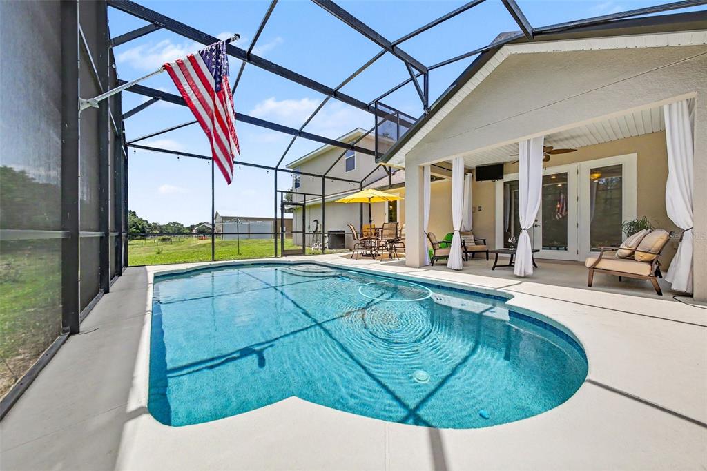 A screened-in pool area features a swimming pool, a covered patio, and an American flag — 11200 BUCKHILL LANE, CLERMONT, FL
