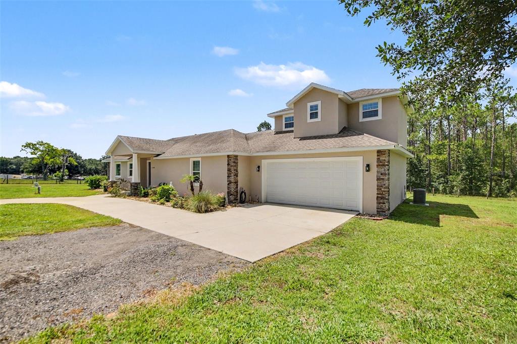 A tan house with a two-car garage and a second-story dormer sits on grass — 11200 BUCKHILL LANE, CLERMONT, FL