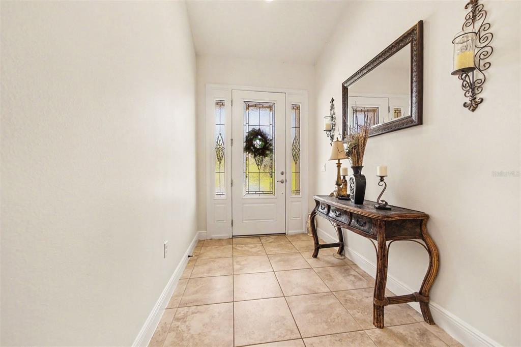 A tiled entryway features a white front door with decorative glass and a wooden console table — 11200 BUCKHILL LANE, CLERMONT, FL