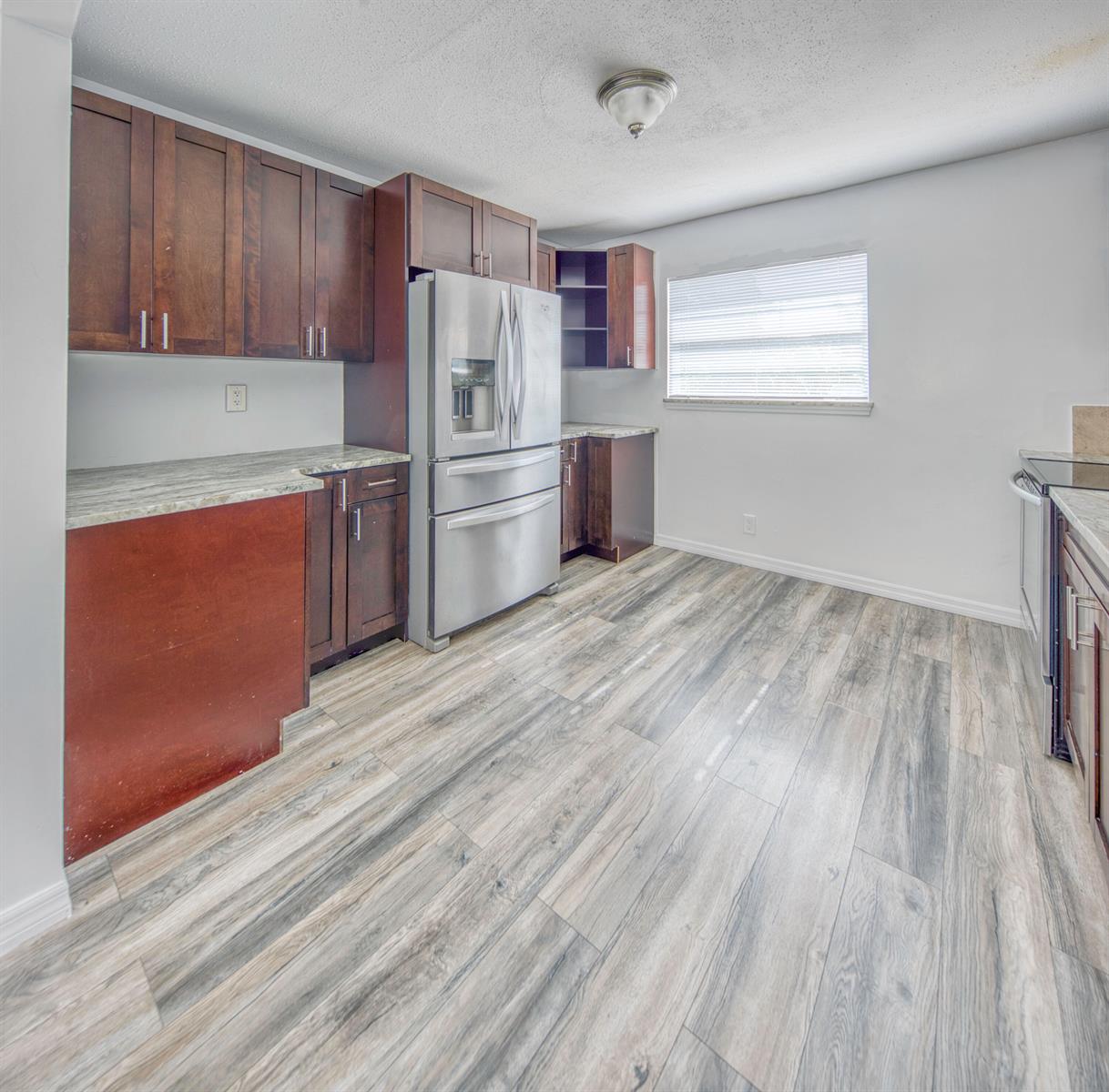 A kitchen features dark wood cabinets, stainless steel appliances, granite countertops, and wood-look flooring — 216 S Ocean Breeze, Lake Worth FL 33460, LAKE WORTH, FL
