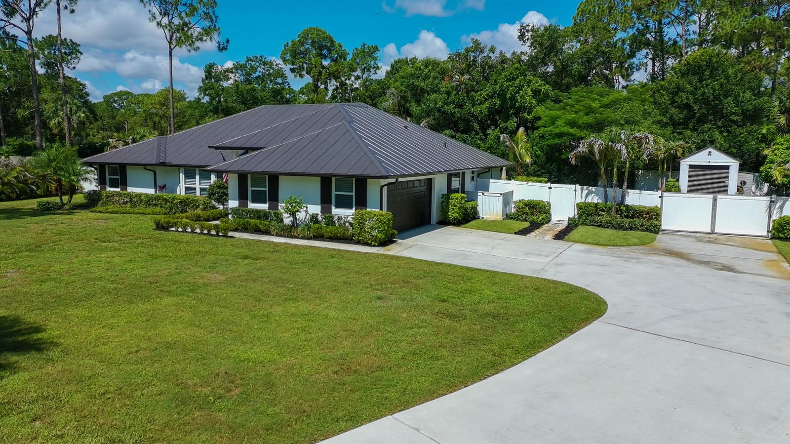 A single-story house with a dark metal roof and a large concrete driveway — 17767 Mellen Lane, Jupiter FL 33478, JUPITER, FL