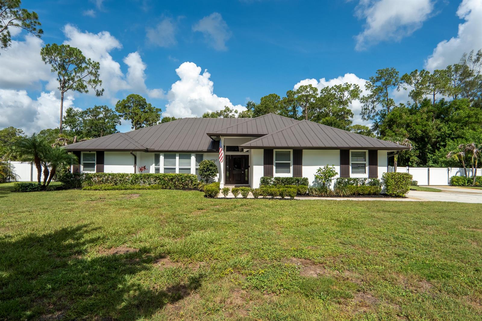 A single-story house with a dark metal roof and white exterior sits on a lawn — 17767 Mellen Lane, Jupiter FL 33478, JUPITER, FL