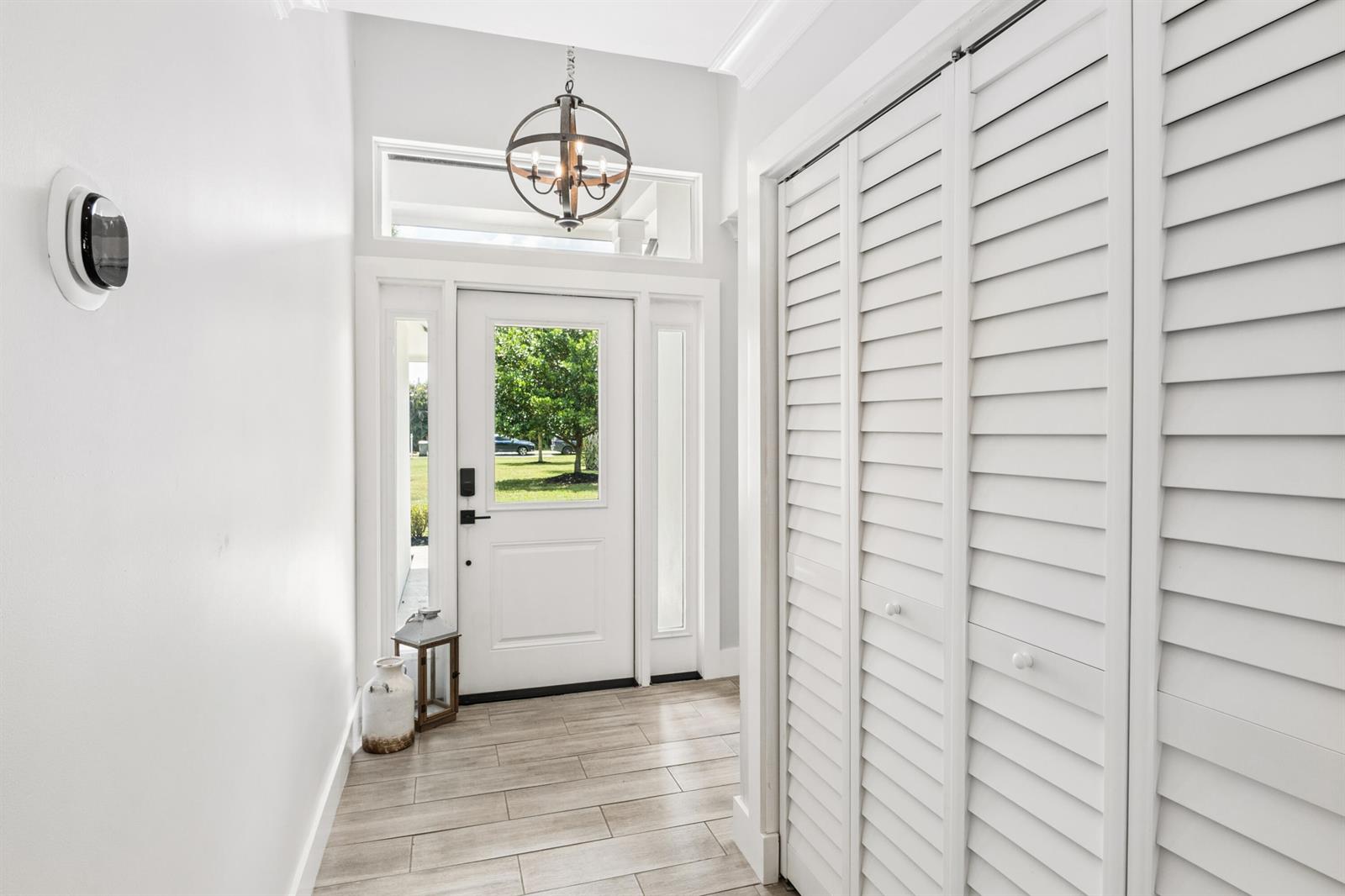 A bright entryway features white louvered closet doors, a globe chandelier, and light wood-look flooring — 17767 Mellen Lane, Jupiter FL 33478, JUPITER, FL