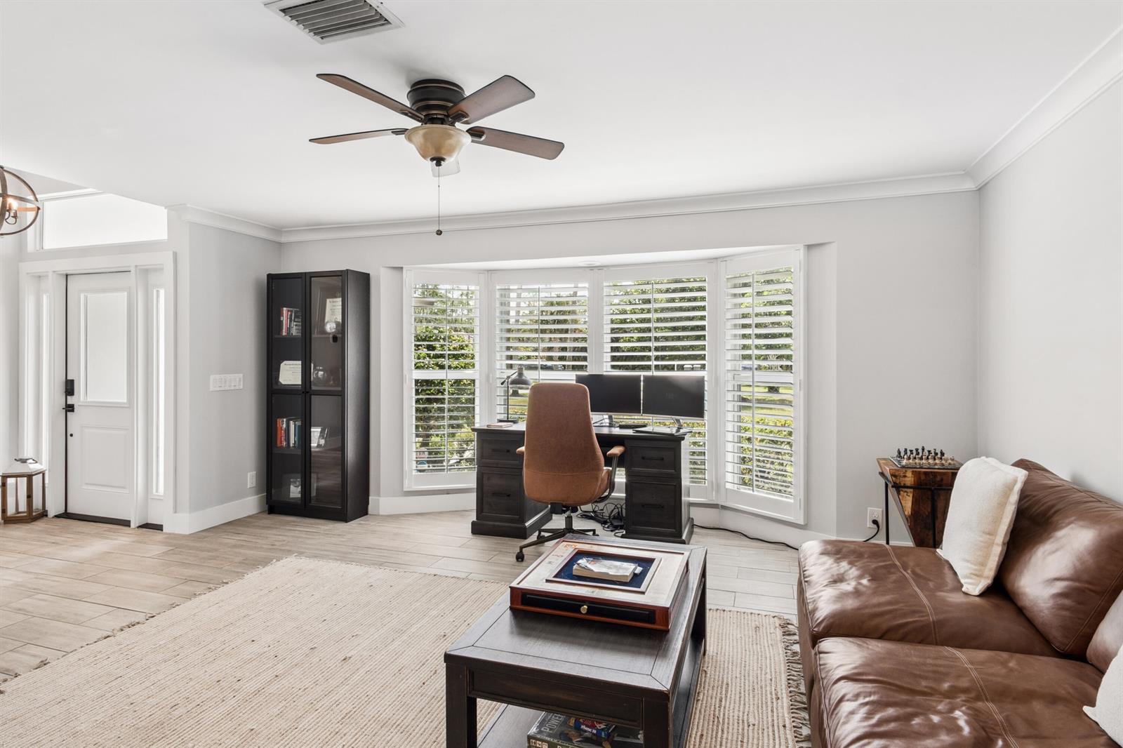 A home office and living area featuring a desk, leather sofa, and bay window shutters — 17767 Mellen Lane, Jupiter FL 33478, JUPITER, FL
