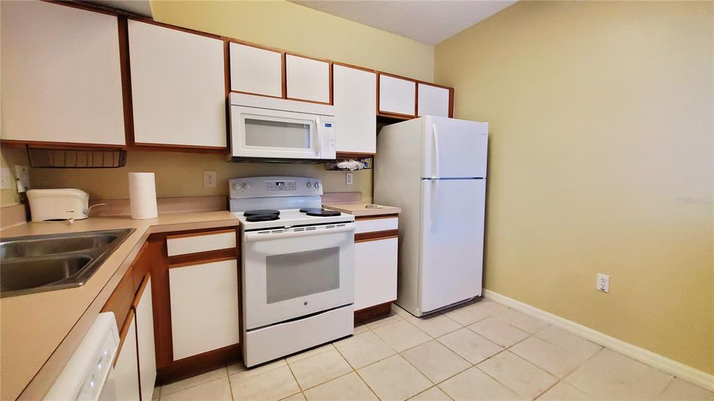 A kitchen features white cabinets, white appliances, a double sink, and light-colored tile flooring — 9612 SEADALE COURT UNIT 101, RIVERVIEW, FL