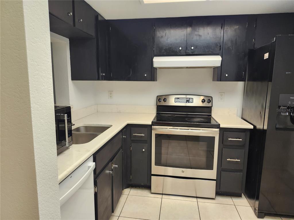 A kitchen features black cabinets, white countertops, stainless steel appliances, and light-colored tile flooring — 2808 60TH AVENUE W UNIT 302, BRADENTON, FL