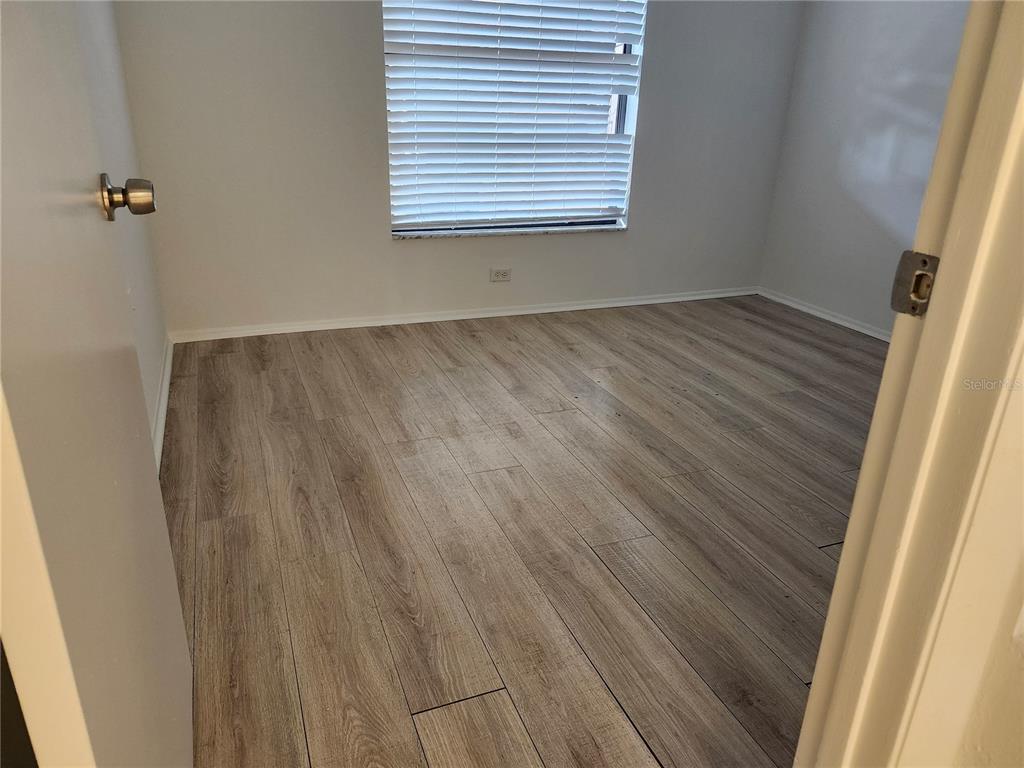 An empty room features light wood-look laminate flooring, white walls, and a window with blinds — 2808 60TH AVENUE W UNIT 302, BRADENTON, FL
