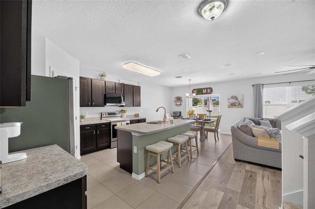 An open-concept kitchen features dark wood cabinets, a central island with bar seating, and tile flooring — 8115 HARWICH PORT LANE, GIBSONTON, FL