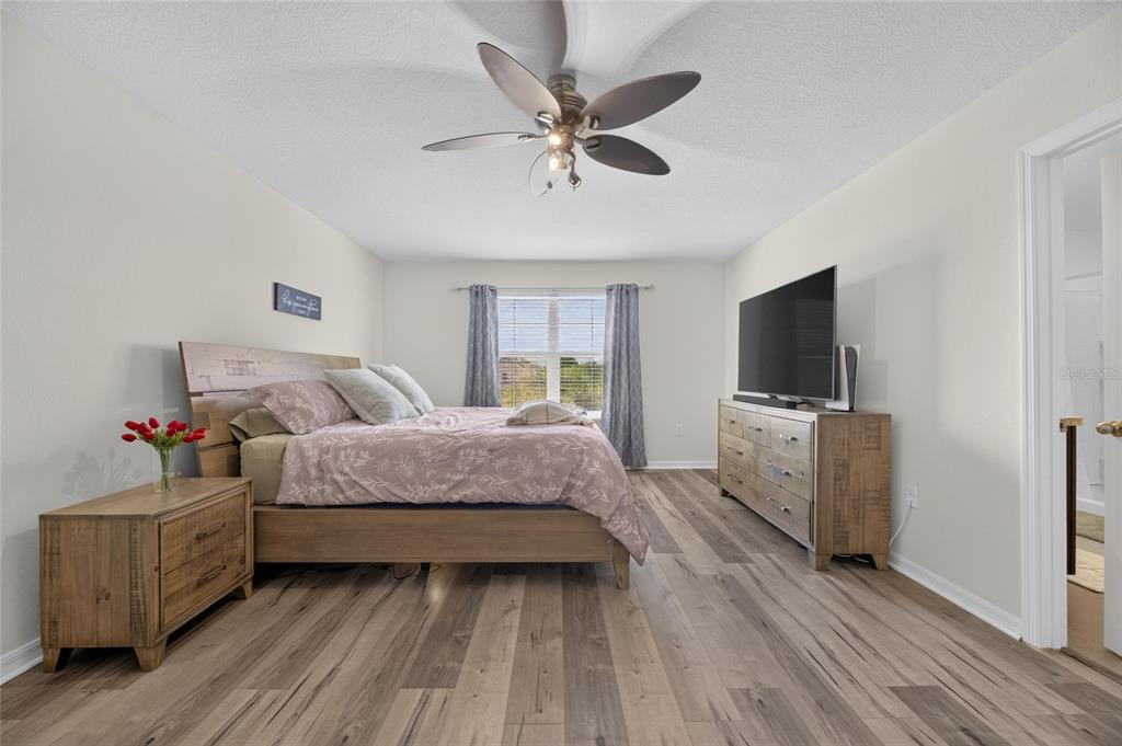 A bedroom features wood-look flooring, a wooden bed frame, a dresser, and a ceiling fan — 8115 HARWICH PORT LANE, GIBSONTON, FL