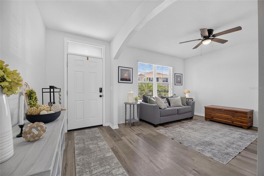 A living room features gray wood-look flooring, a gray sofa, and a wooden storage chest — 8115 HARWICH PORT LANE, GIBSONTON, FL