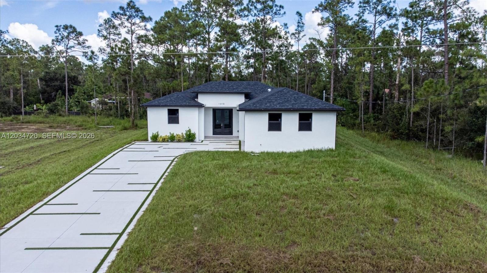 A modern white single-story house with a dark roof stands on a grassy lot — 1310 Jefferson Ave, Lehigh Acres FL 33972, LEHIGH ACRES, FL