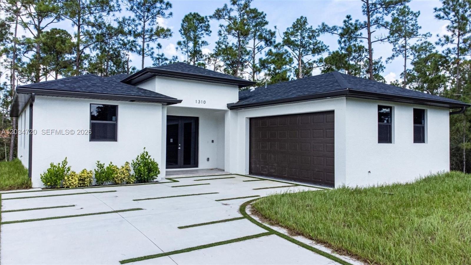 A modern white house with a dark roof and garage sits behind a concrete driveway — 1310 Jefferson Ave, Lehigh Acres FL 33972, LEHIGH ACRES, FL
