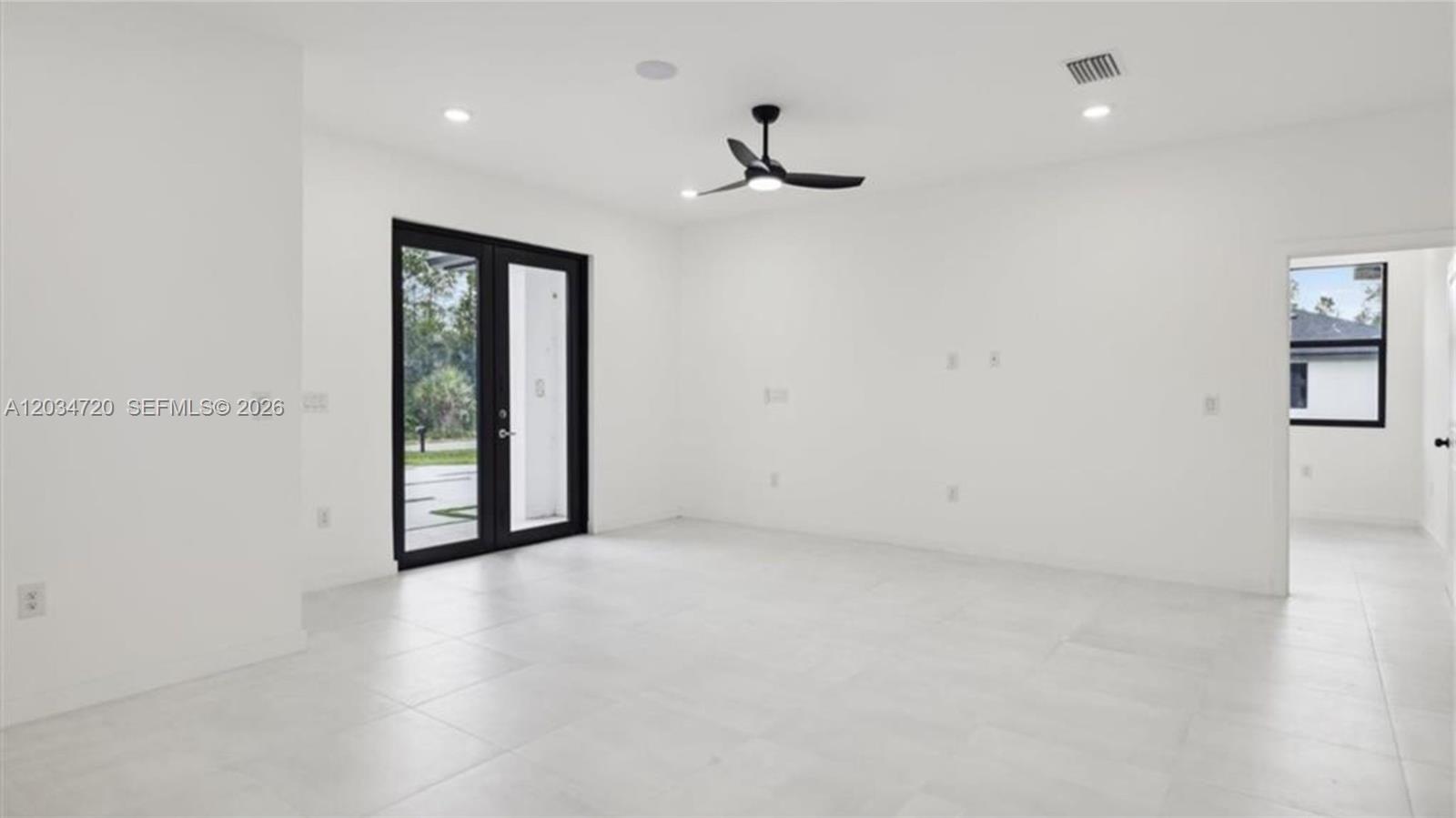 A bright, minimalist room features white walls, tile flooring, a ceiling fan, and glass doors — 1310 Jefferson Ave, Lehigh Acres FL 33972, LEHIGH ACRES, FL