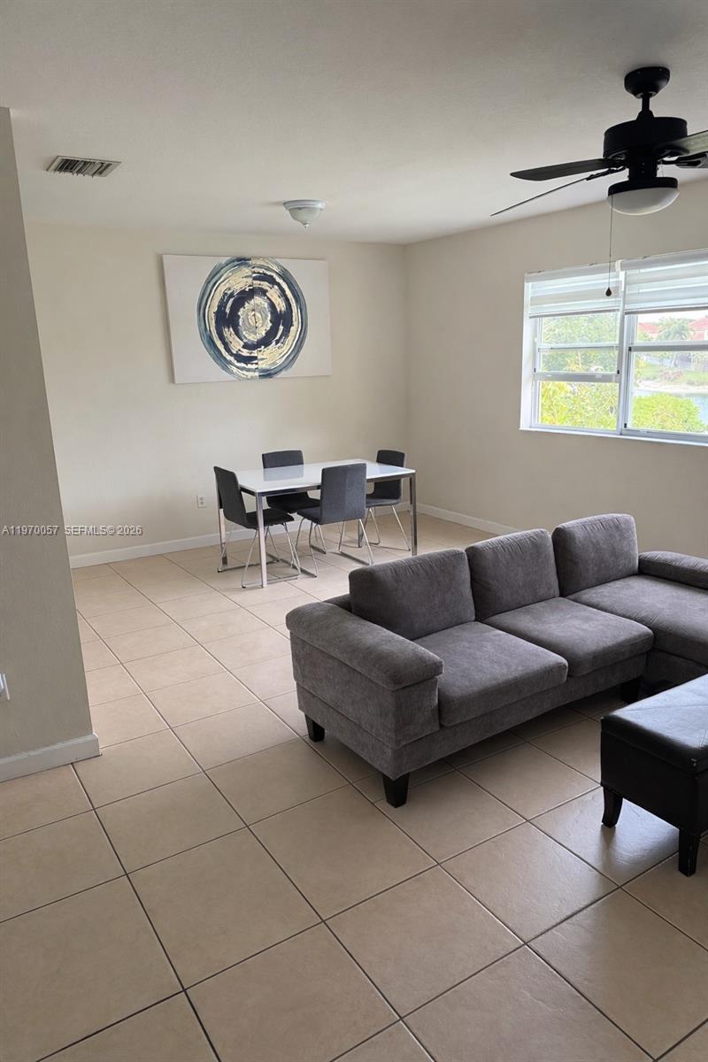 This living and dining area features tile flooring, a gray sectional sofa, and a ceiling fan — 1485 NE 33rd Rd # 207, Homestead FL 33033, HOMESTEAD, FL