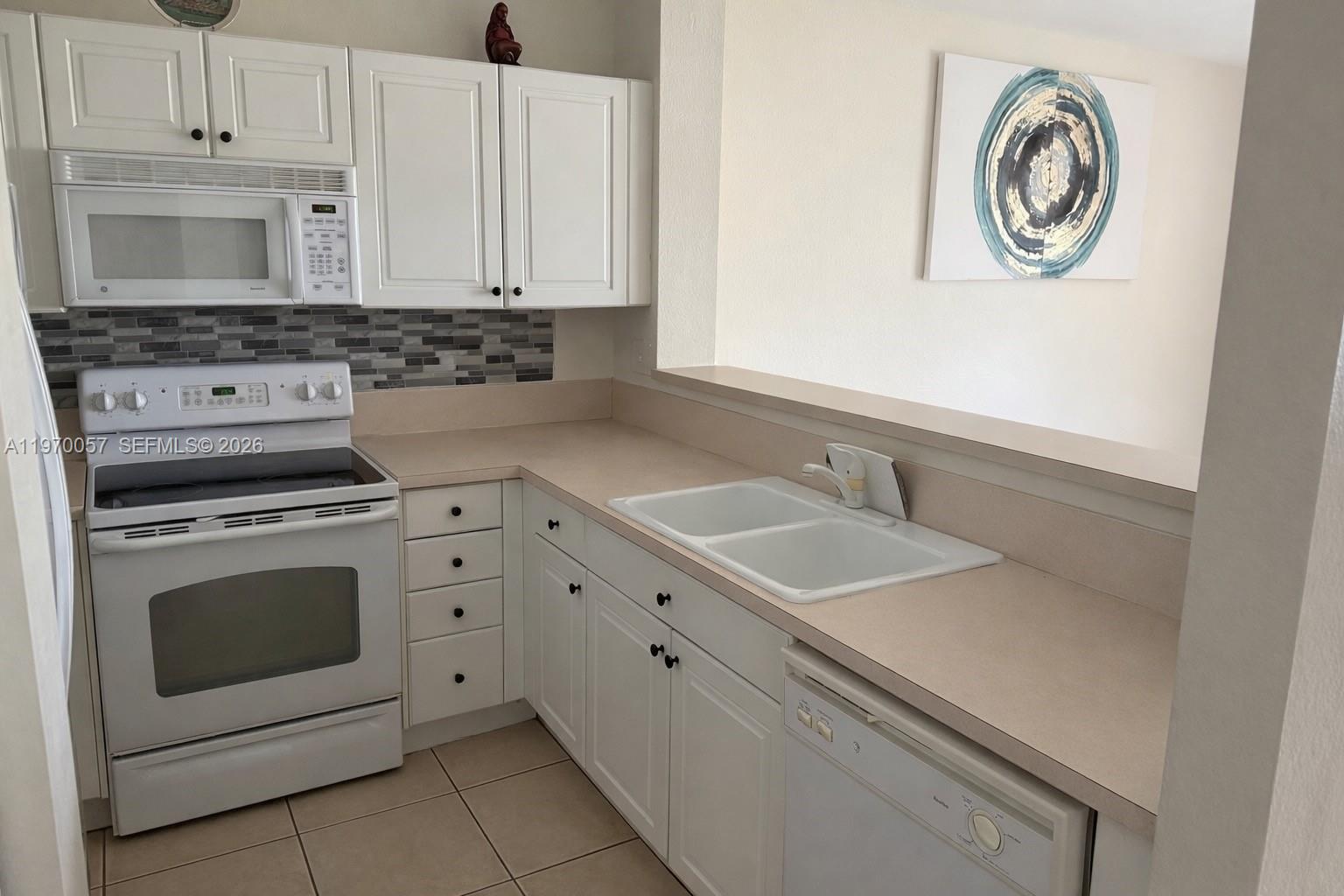 A kitchen features white cabinets, a white stove, a double sink, and a tiled backsplash — 1485 NE 33rd Rd # 207, Homestead FL 33033, HOMESTEAD, FL