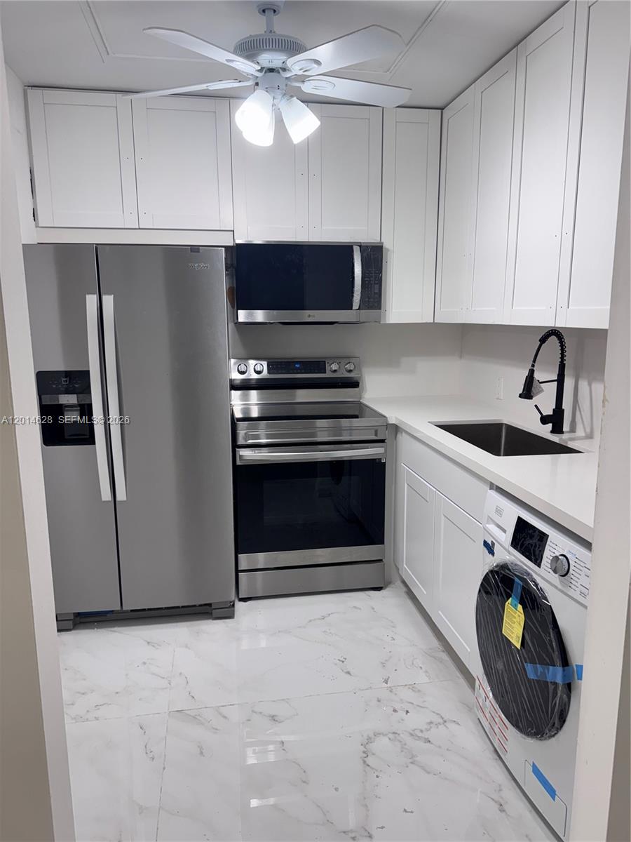 A small kitchen features white cabinets, stainless steel appliances, a washer, and marble-look tile flooring — 272 Dorset # G, Boca Raton FL 33434, BOCA RATON, FL