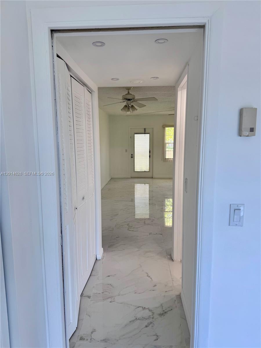 A hallway with white marble-style flooring leads toward a room with a ceiling fan — 272 Dorset # G, Boca Raton FL 33434, BOCA RATON, FL