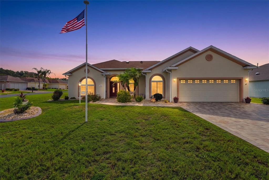 A single-story house with a beige stucco exterior, a two-car garage, and an American flag — 17790 SE 125TH CIRCLE, SUMMERFIELD, FL