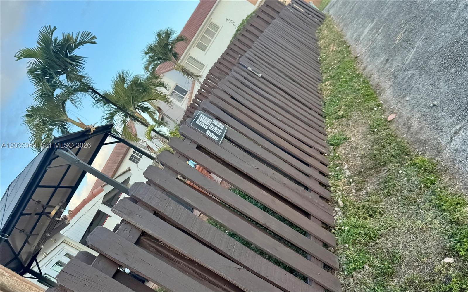 A wooden fence with a warning sign stands beside a paved path and palm trees — 13326 SW 9th Ter, Miami FL 33184, MIAMI, FL