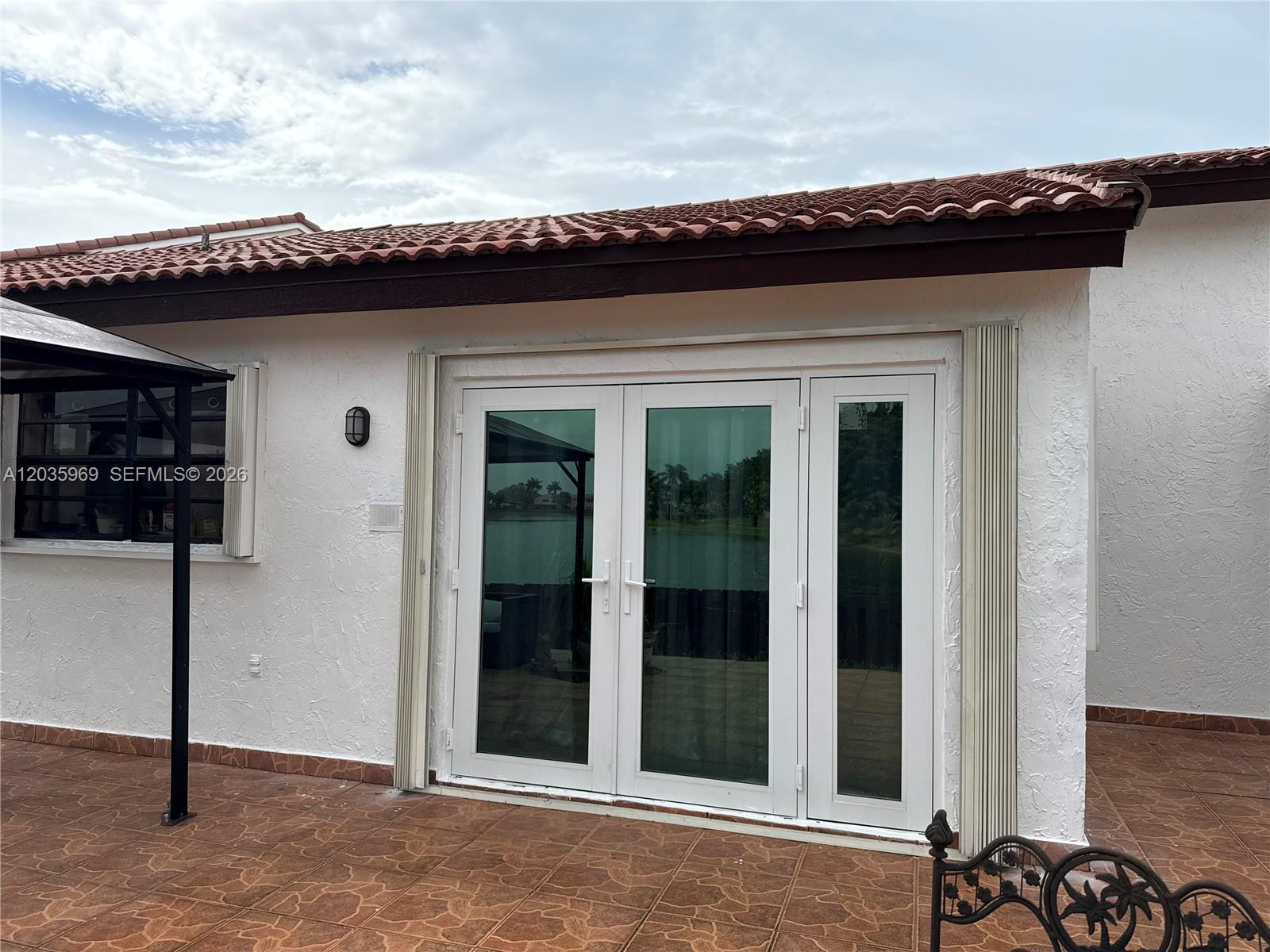 A white house exterior features a set of glass French doors and a tiled patio — 13326 SW 9th Ter, Miami FL 33184, MIAMI, FL