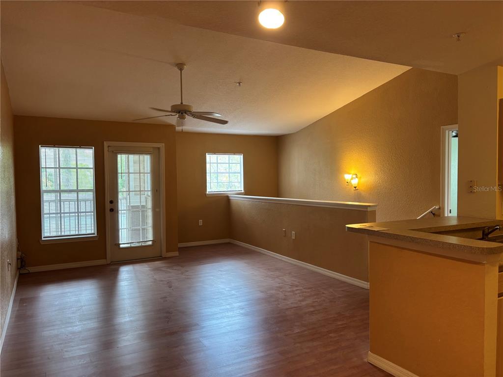 A living room features wood-look flooring, a vaulted ceiling with a fan, and a balcony door — 7411 VISTA WAY UNIT 203, LAKEWOOD RANCH, FL