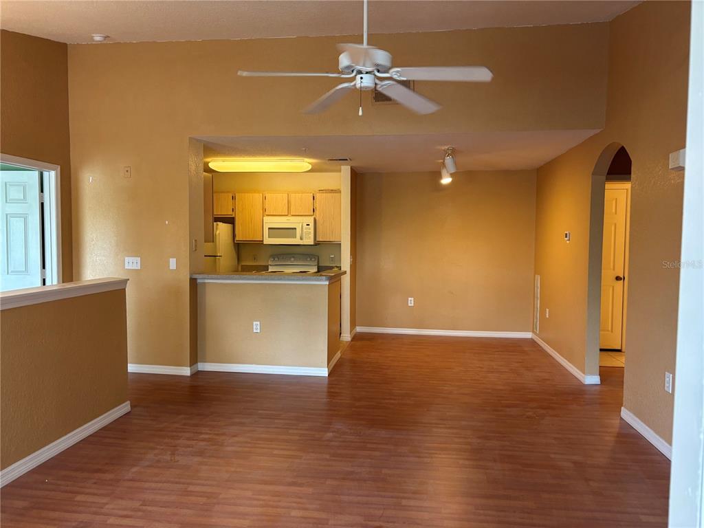 An open-concept living area features wood-look flooring, tan walls, and a kitchen with light-colored cabinets — 7411 VISTA WAY UNIT 203, LAKEWOOD RANCH, FL