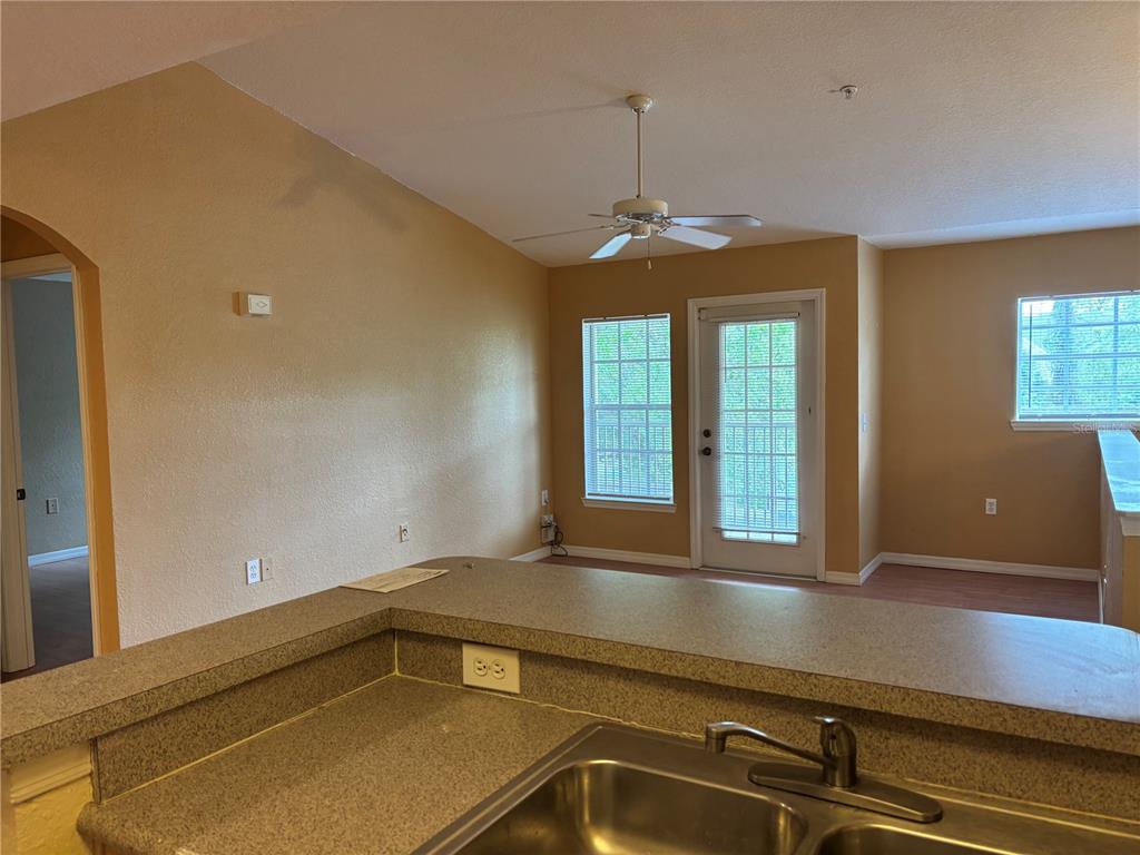 A kitchen sink and countertop overlook a living area with a ceiling fan and door — 7411 VISTA WAY UNIT 203, LAKEWOOD RANCH, FL